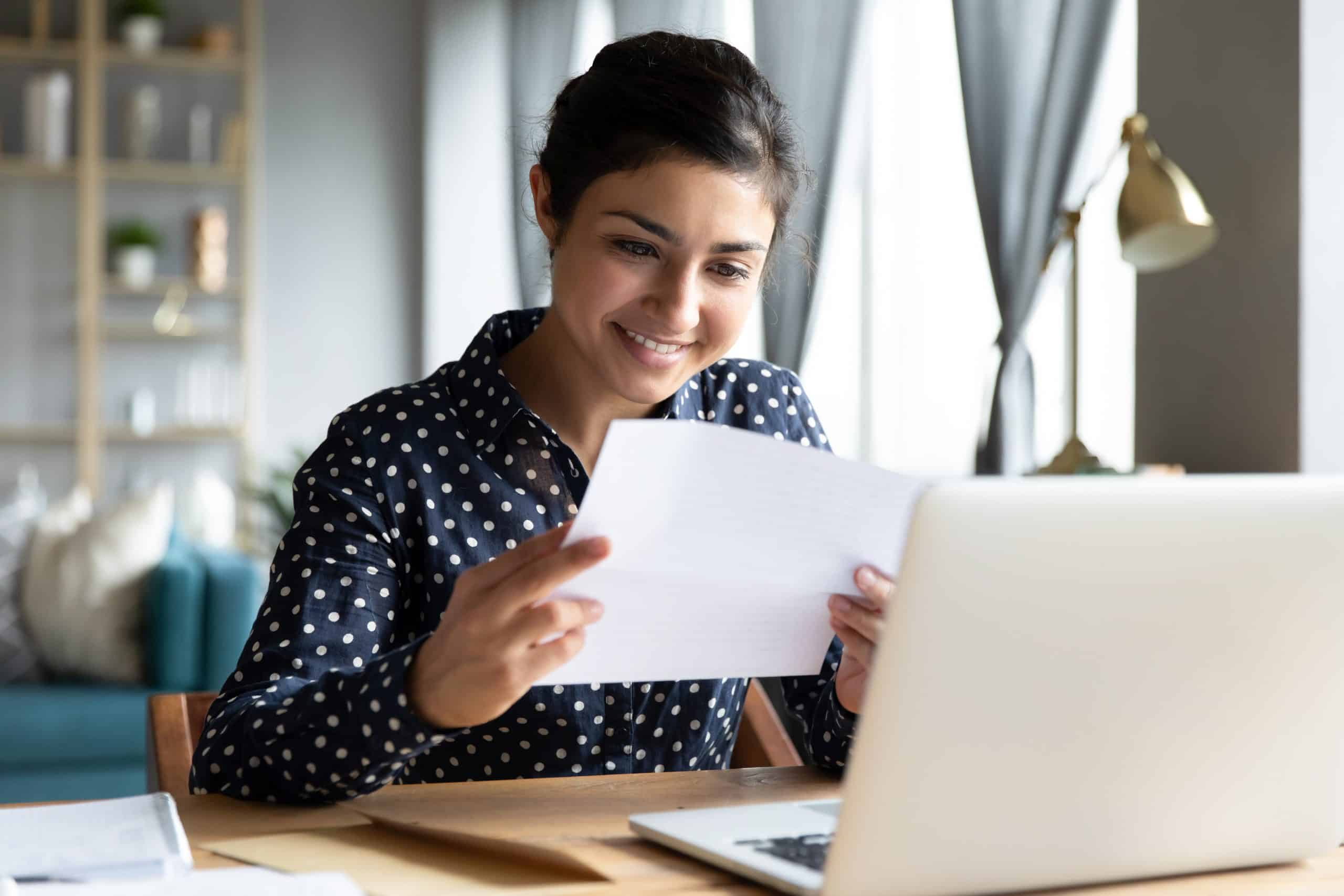 Smiling indian woman holding reading paper letter sit at table